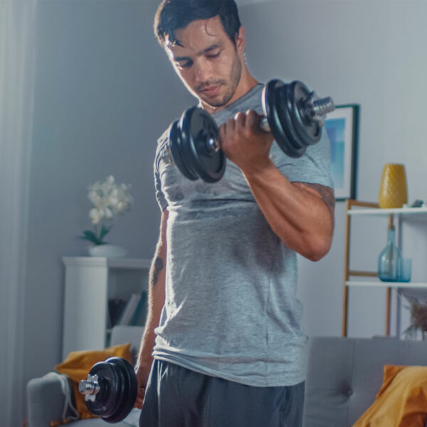 Sportlicher Mann trainiert mit einem Kurzhantel-Set aus Gusseisen in seinem Wohnzimmer.